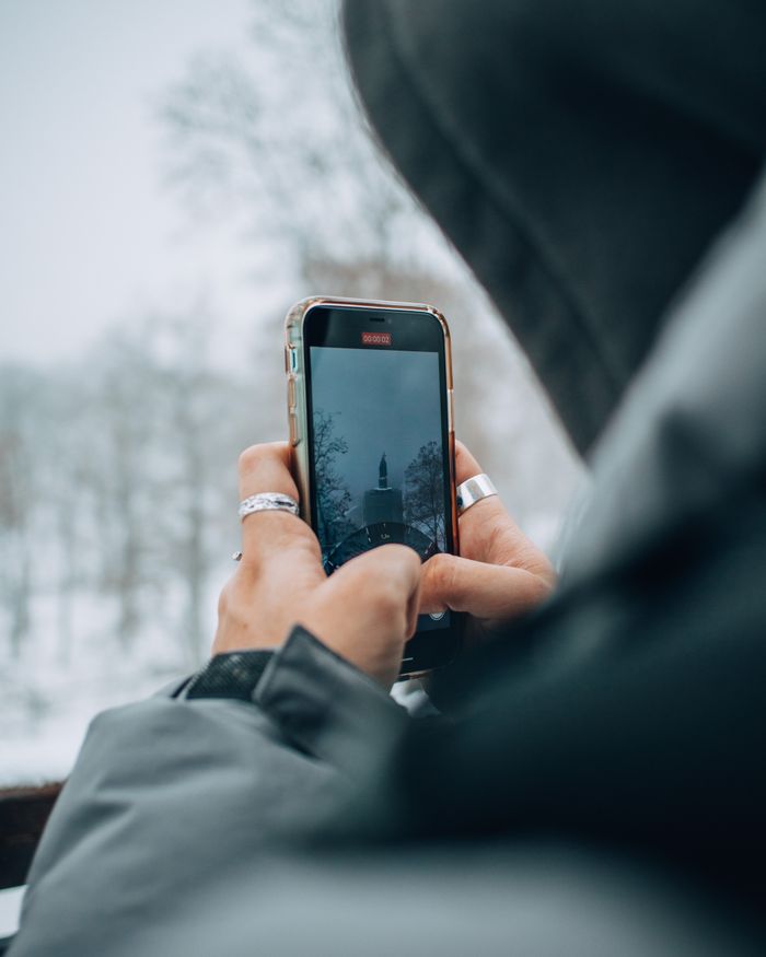 A person capturing a winter scene in Kyiv, Ukraine, using a smartphone amidst snowy trees.